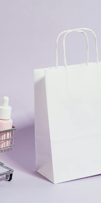 A minimalist image featuring a shopping cart with cosmetics and a white paper bag, ideal for Black Friday promotions.