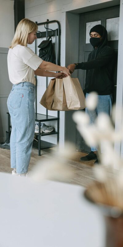 A woman receives a delivery package from a courier at her doorstep inside a modern home.