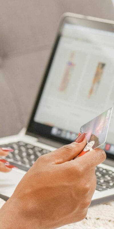 A woman relaxes on a couch while shopping online using her laptop and credit card.