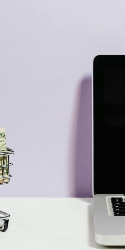Shopping cart with money next to a laptop symbolizing online shopping and e-commerce.